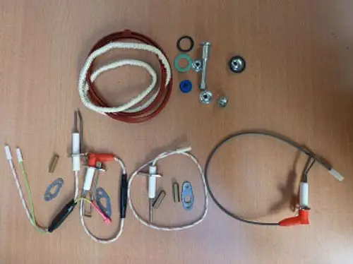 Remeha Wartungssatz mit verschiedenen Komponenten, darunter Kabel, Stecker, Unterlegscheiben und andere Bauteile, die auf einer Holzoberfläche angeordnet sind.